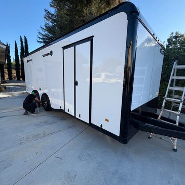 A person working on the wheel of a white and black trailer parked on a driveway.