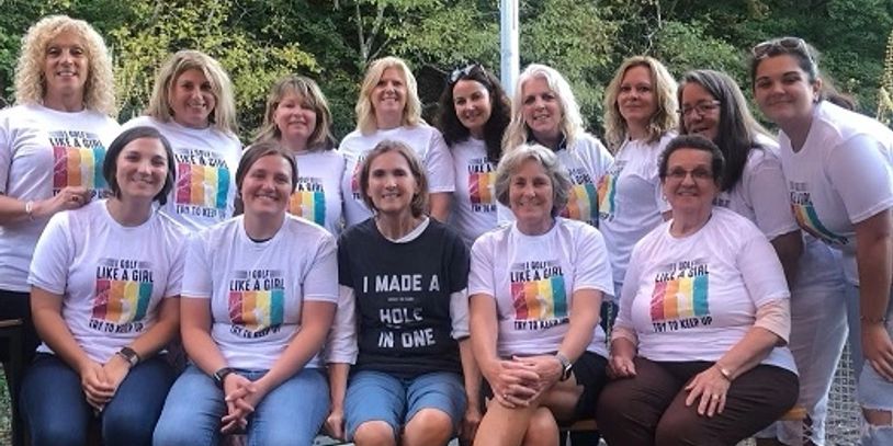 Group of women wearing golf-themed shirts posing outdoors.