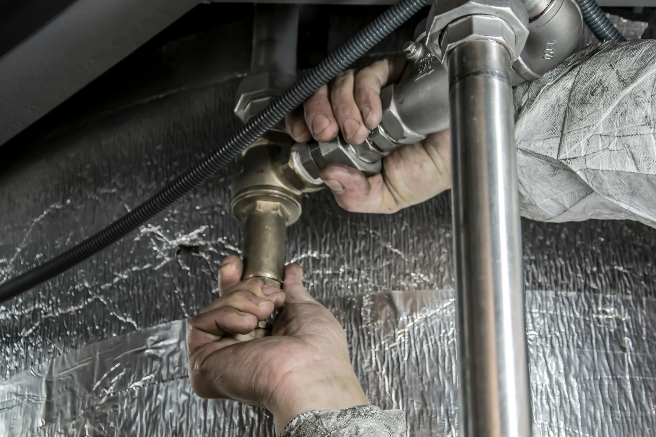 Close-up of a worker fixing plumbing pipes under a sink.