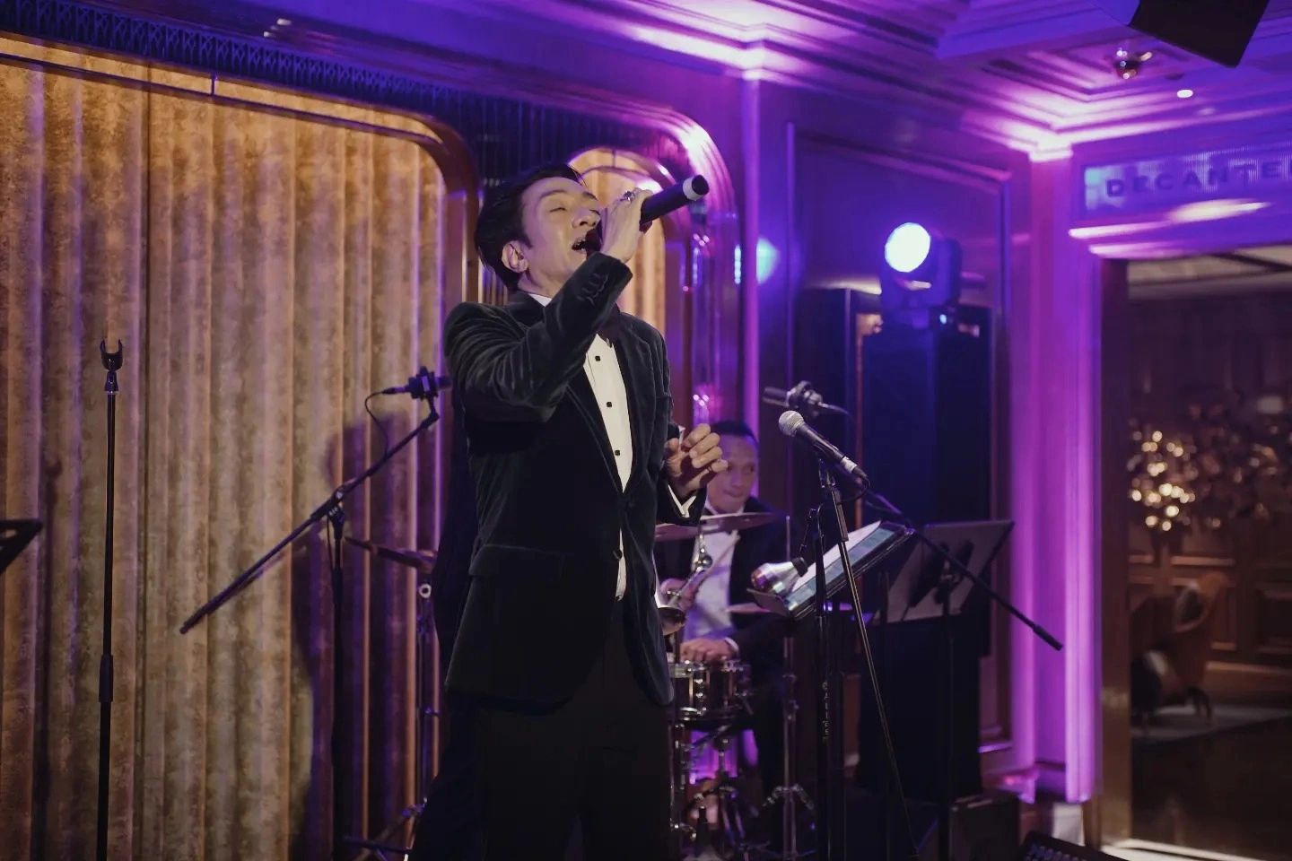 Man singing on stage in a suit and hat.