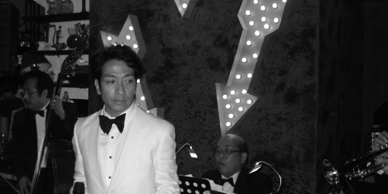 Man in white tuxedo singing with jazz band.