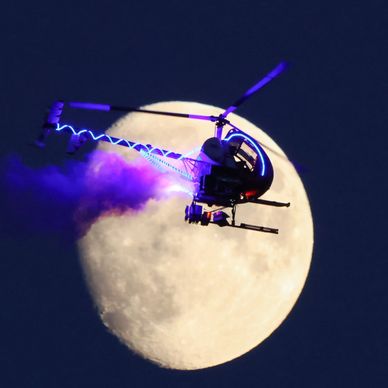 Helicopter flying in front of the full moon with colored lights.