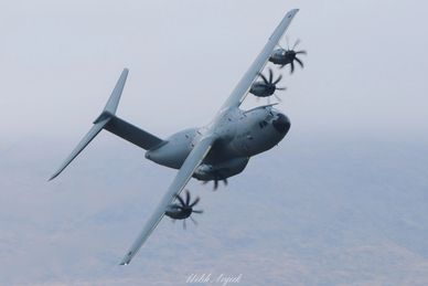 Military cargo plane banking in the sky with four propellers spinning.