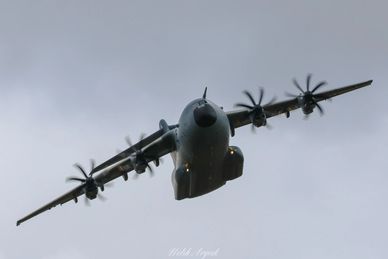 Military transport aircraft flying against a cloudy sky.