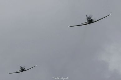 Two small planes flying against a cloudy gray sky.