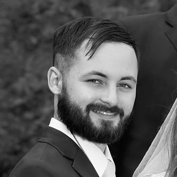 A smiling man with a beard in a suit at an outdoor event.