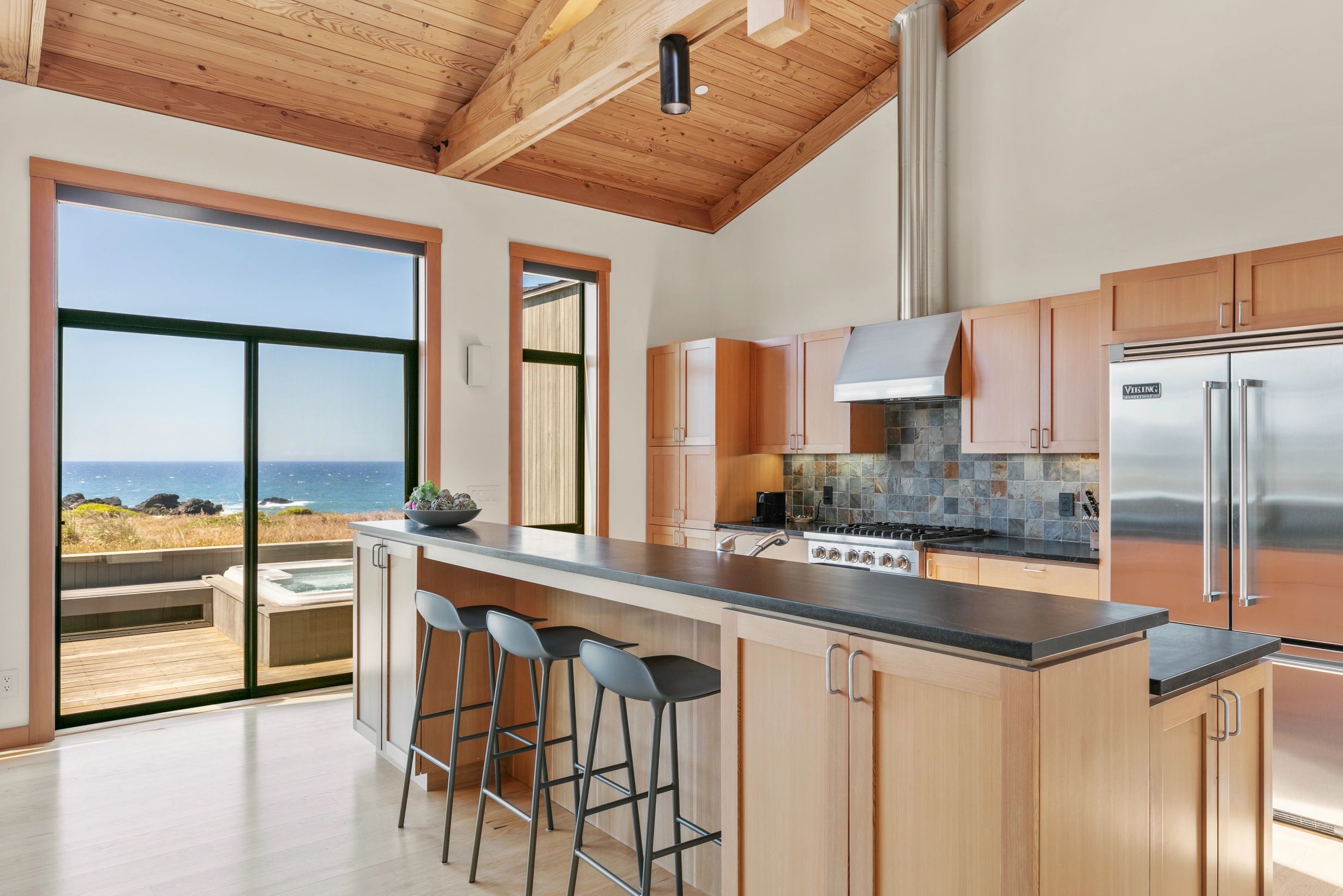 Modern kitchen with ocean view and wooden ceiling.
