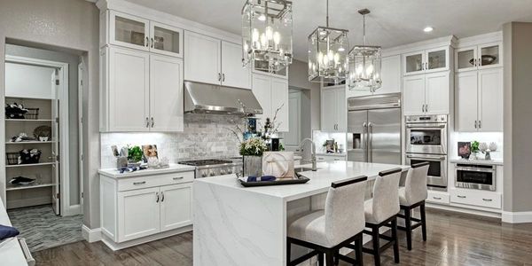 Modern white kitchen with marble island and pendant lights.