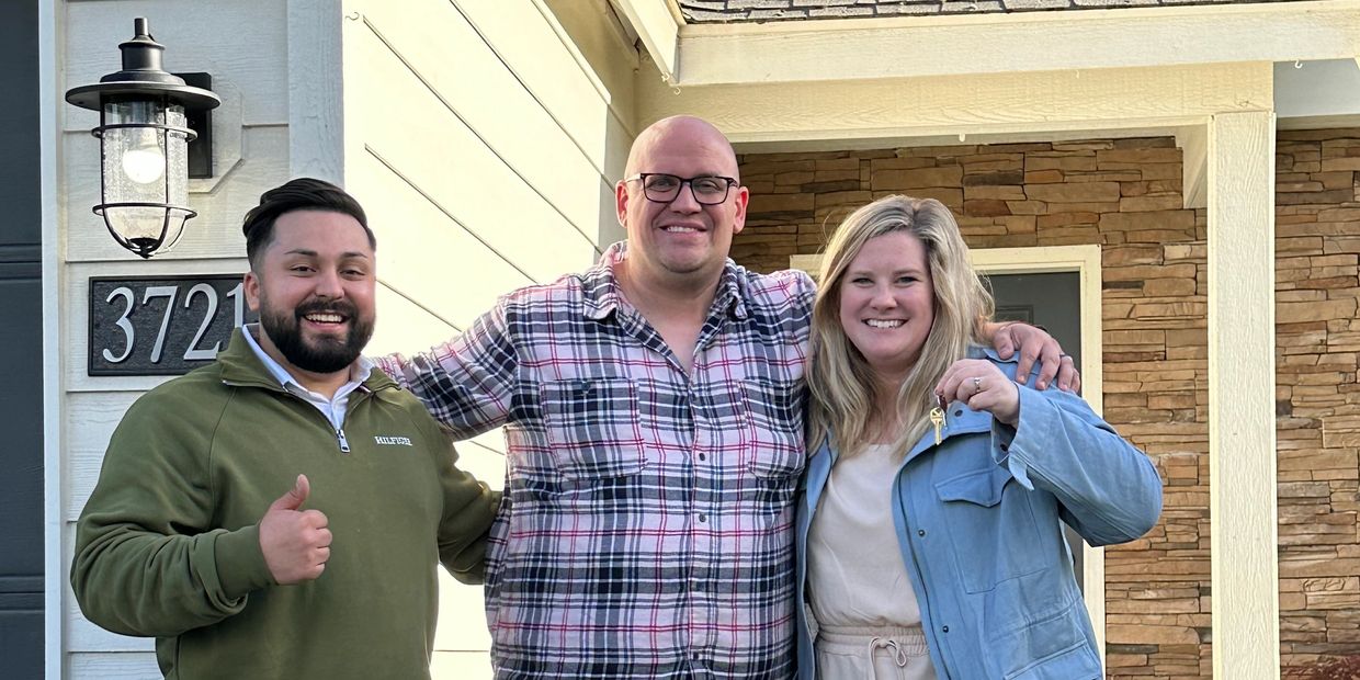 Three people smiling in front of a house, one holding keys.