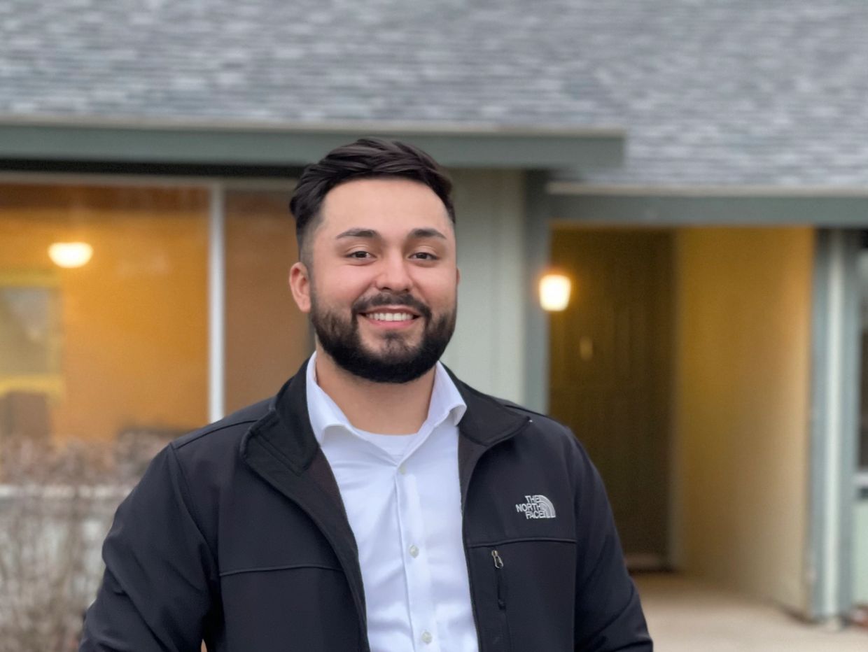 Smiling man in a black jacket standing outdoors.