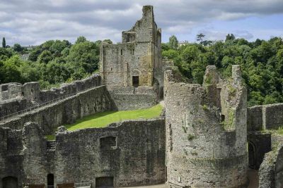 Ancient stone castle ruins surrounded by lush greenery under a cloudy sky.