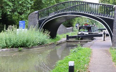 A narrowboat passing under a brick and iron bridge on a canal.