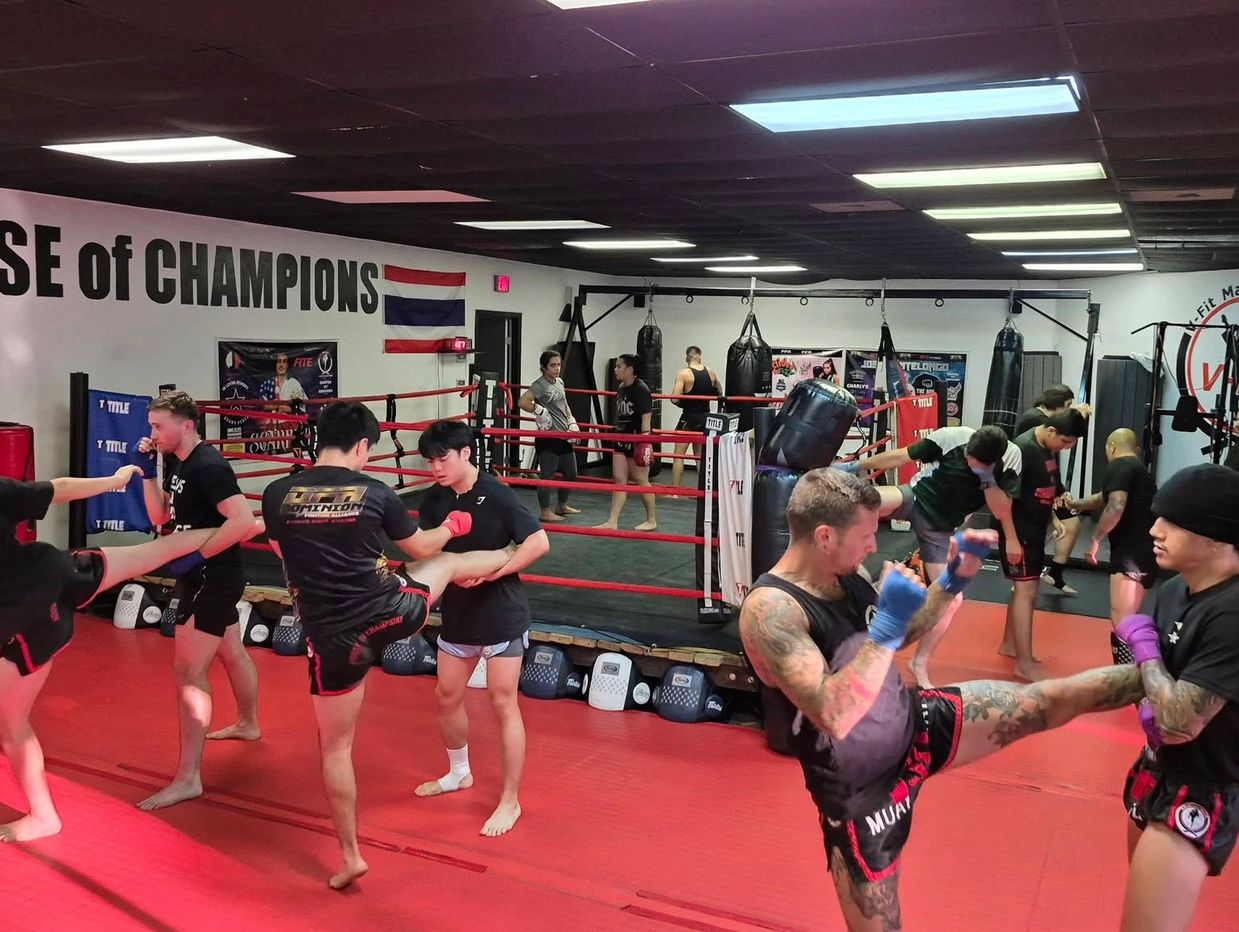 People practicing kickboxing in a gym with a boxing ring.