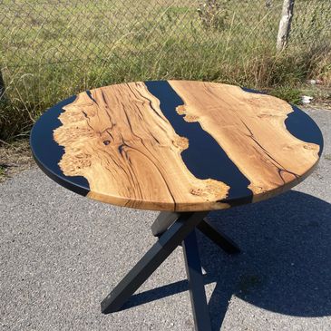 Round wooden table with black resin inlays and metal legs.