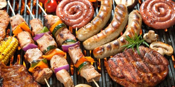 Grilled sausages, meat skewers, and vegetables cooking on a barbecue grill.