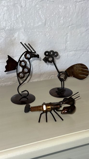 Metal sculptures of a seahorse, a bird, and a lobster on a table.