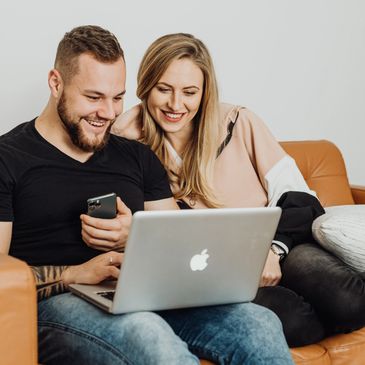 Man and woman smiling, sitting on couch looking at their laptop