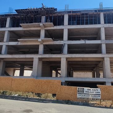 İnşaat halinde boş beton bina ve önünde satılık kutu daire ilanı.