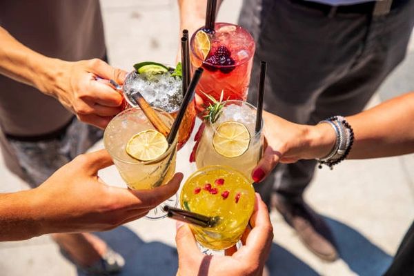 Friends clinking colorful cocktails outdoors on a sunny day.
