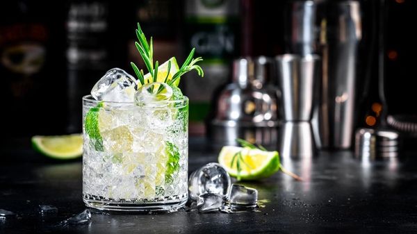 Refreshing cocktail with lime, ice, and rosemary garnish on a dark bar counter.