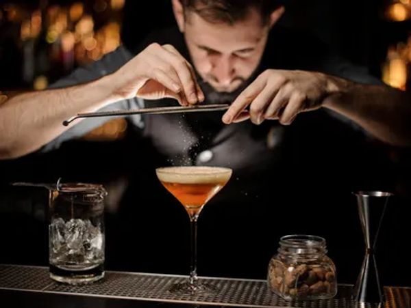 Bartender grating garnish over cocktail in dimly lit bar.