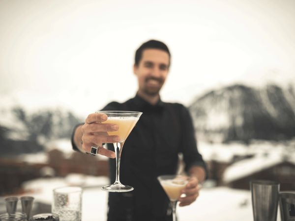 Bartender offering a cocktail with snowy mountains in the background.