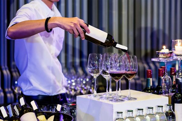 A person pours red wine into glasses at a bar or event.