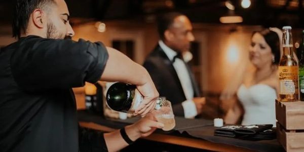 Bartender pouring a drink while a couple talks in the background.