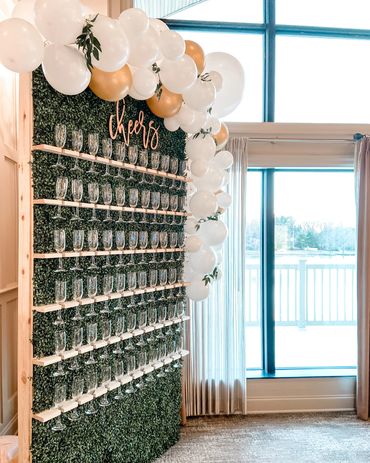 Image is of a green champagne wall with 6 rows of champagne glasses hanging on it. 