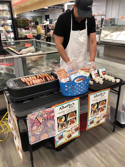 Man grilling sausages at a food sampling booth in a grocery store.