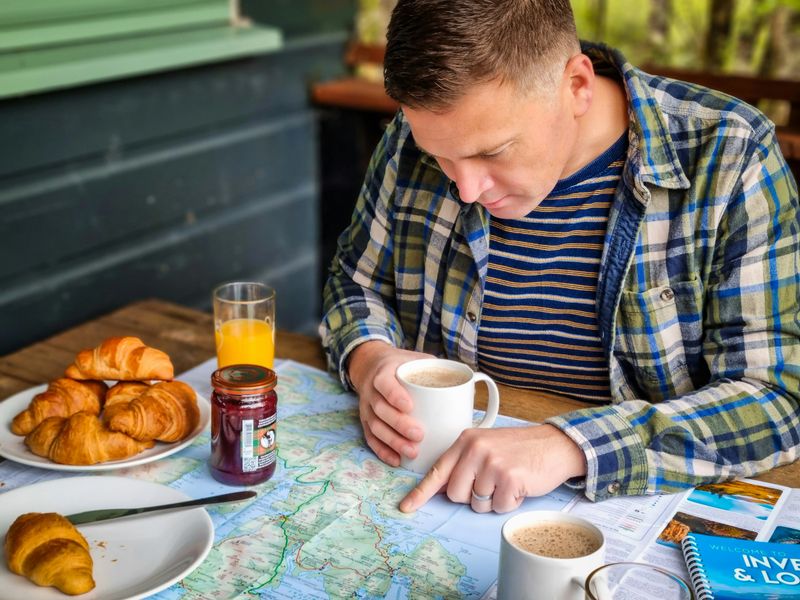 Travel planning scene with map, coffee, and croissants—person exploring destinations and planning a trip with guidebooks and itinerary.