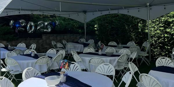 White chairs and tables set up under a tent for a 2023 event.
