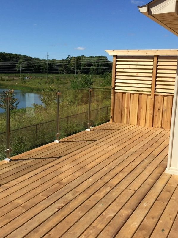 Wooden deck with glass railing overlooking a green landscape and pond.