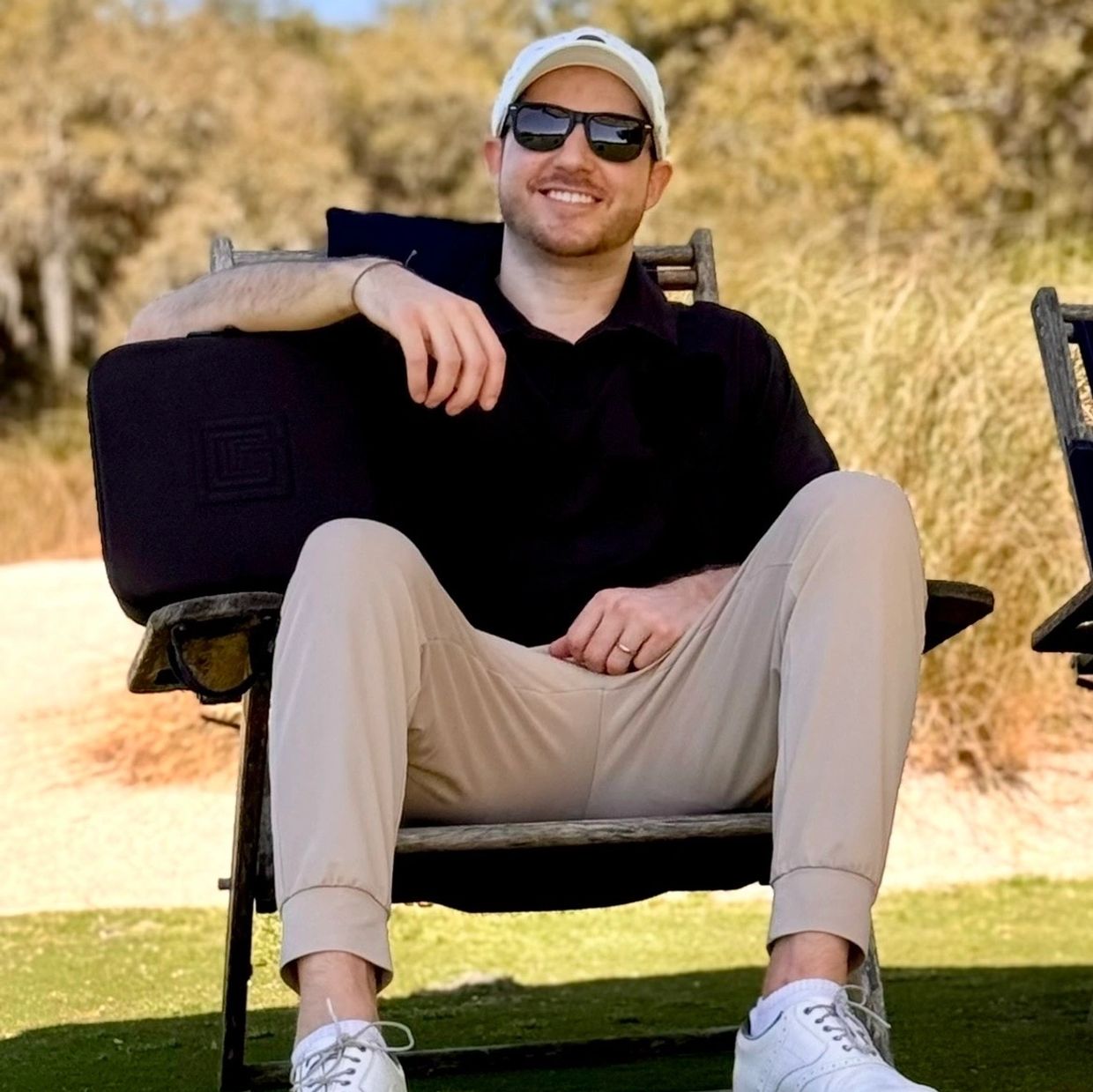 Man in casual outfit relaxing outdoors on a chair with sunglasses and a cap.