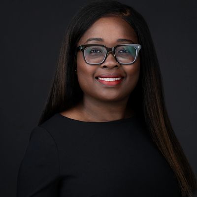 Professional portrait of a smiling woman with glasses and long hair against a black background.