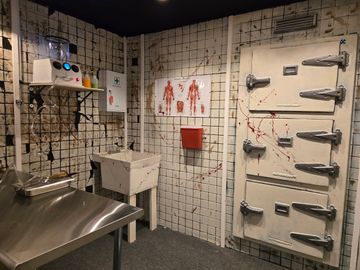 A creepy, blood-splattered morgue room with a body chart and heavy metal doors.