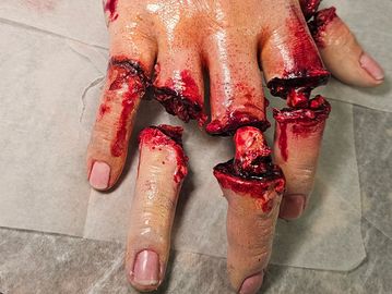 A realistic special effects hand with severed fingers and blood.