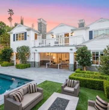 Elegant white two-story house with outdoor seating and pool at sunset.