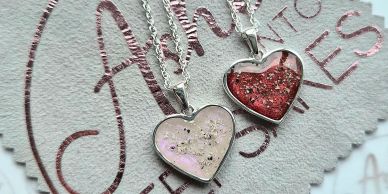 Two heart-shaped pendant necklaces on a textured surface.