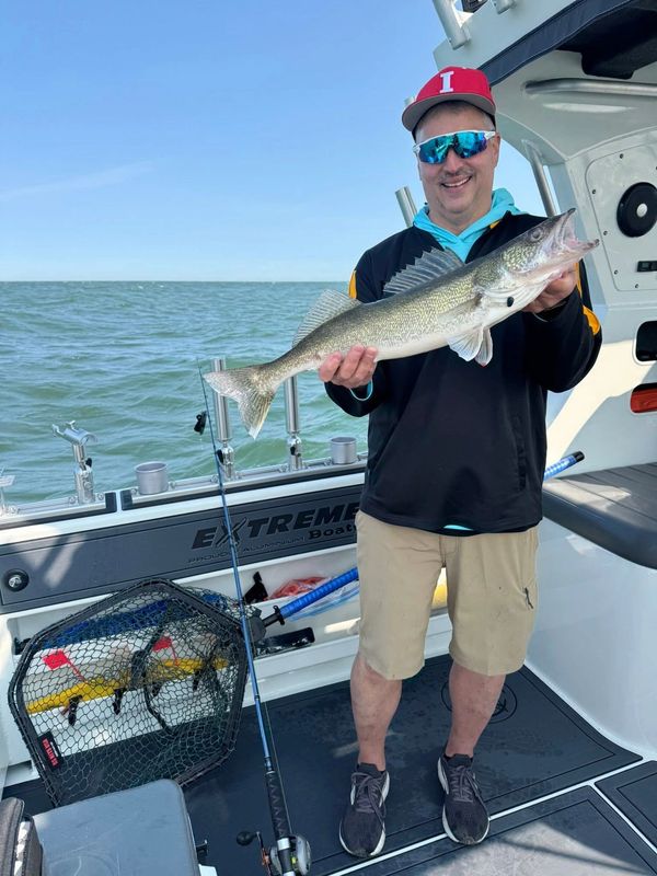 Man holding a fish on a boat with water in the background.
