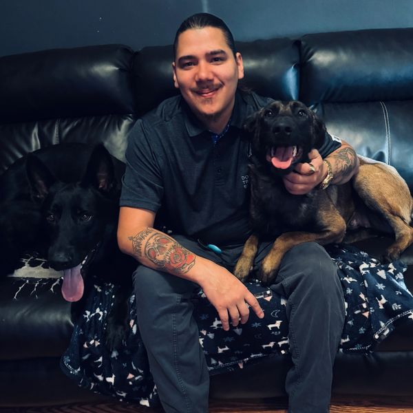 Man with tattoos sitting on a couch with two happy dogs.