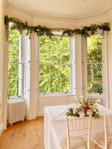 Bright room with large windows, greenery outside, and a decorated table with flowers.