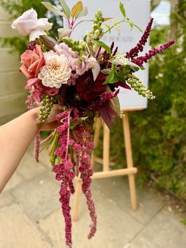 Hand-held bouquet with mixed flowers and cascading pink elements.