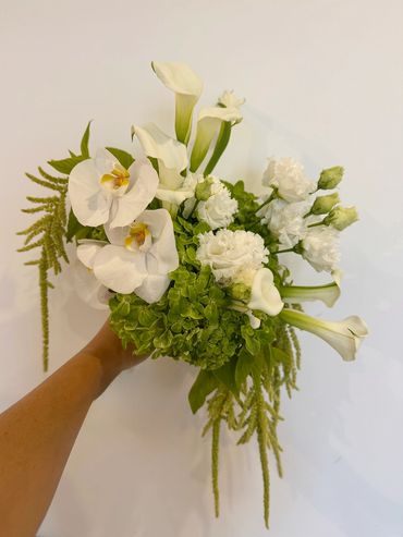 Hand holding elegant white and green floral bouquet.