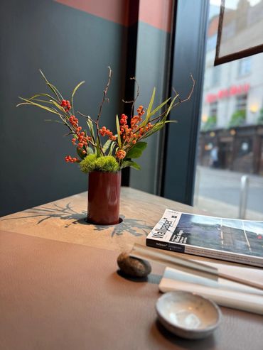 Elegant flower arrangement in a red vase on a table by the window.