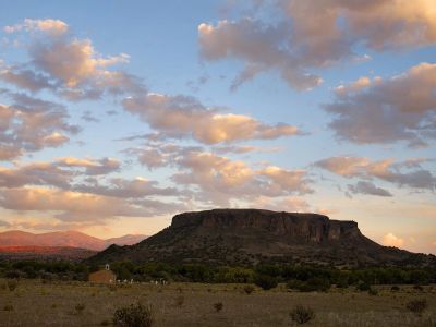 A flat-topped mountain at sunset with scattered clouds and a small building in the foreground.
