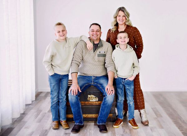 A smiling family of four posing indoors on a wooden floor.