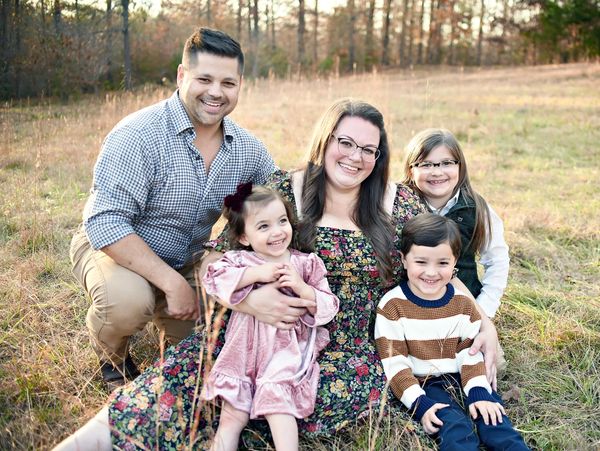 Smiling family of five enjoying a sunny day outdoors in a grassy field.
