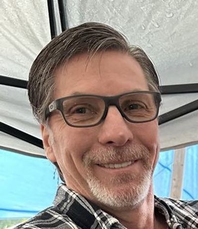 Middle-aged man wearing glasses and a checkered shirt, smiling.