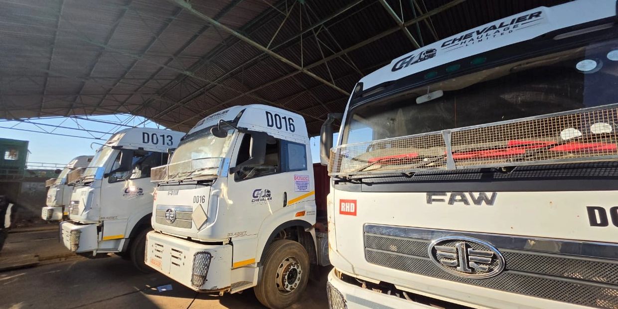 Three white FAW trucks parked inside a warehouse under a metal roof.